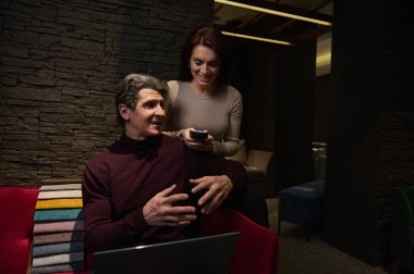 Yeni ev tasarımı projesinde çalışan deneyimli iç mimarlardan oluşan yaratıcı bir ekip, koltuğun arkasında döşeme kumaşı örnekleri ile kırmızı koltukta oturuyorlar.