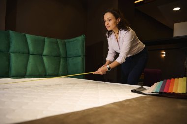 Çekici bir kadın, iç mimar, bir mobilya mağazasında satış müdürü ortopedik bir yatak ve döşeme tekstili için yumuşak bir yatak ölçüleri alıyor. Ev tasarımı kavramı