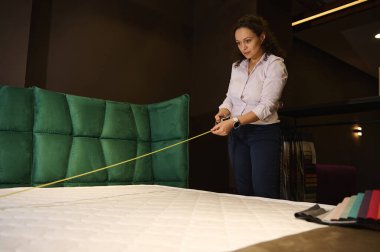 Ölçüm bandı kullanan yaratıcı profesyonel dekoratör ve iç mimar, döşeme kumaşlarının daha fazla seçilmesi için ortopedik yatak ve döşemelerden ölçümler alıyor