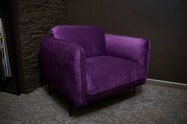 An exhibition of a stylish comfortable purple velour armchair dispalyed for sale in a furniture design showroom. Upholstered furniture store, home design concept