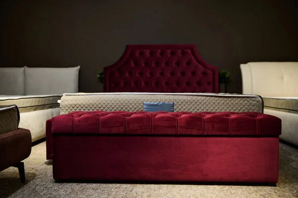 Comfortable stylish red upholstered bed with orthopedic mattress and velour ottoman, displayed for sale in a furniture design showroom. Bedroom interior design