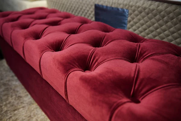 Focus on a red velour footstool, ottoman dispayed for sale in a furniture store