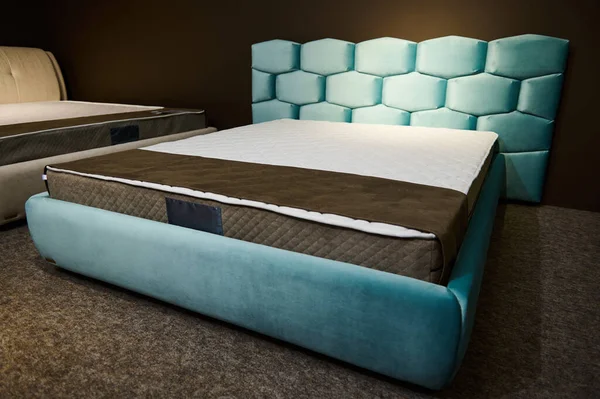 Angle view of a comfortable modern stylish velour turquoise double beds with orthopedic hard mattresses, displayed for sale in the showroom of a furniture design store