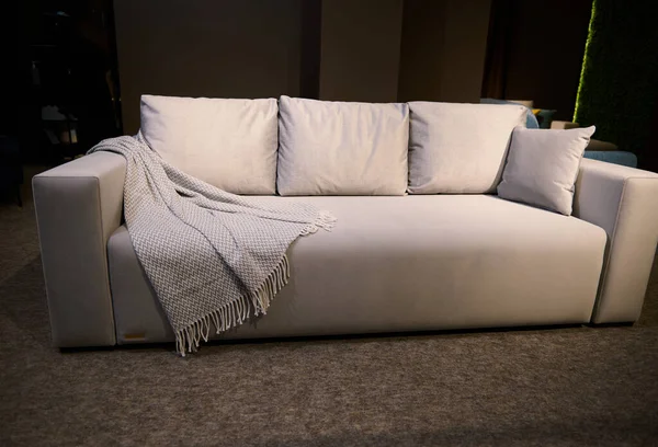 クッションとベージュのブランケットを備えたスタイリッシュなミニマリストで快適なソファは ホームデザインスタジオで販売されています 家具屋 インテリアデザイン 化粧品のコンセプト — ストック写真