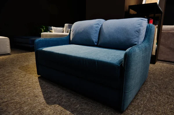 Interior of furniture salon. Simple and minimalist navy blue sofa, settee, couch displayed for sale in home design store. Home interior design, inprovement and decoration cosiness concept