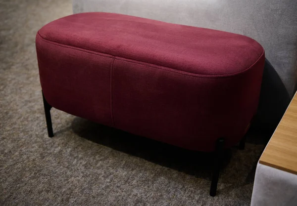 Stylish comfortable long red velour ottoman or footstool in the exposition hall of a furniture store. Interior design, cosiness and home improvement concept