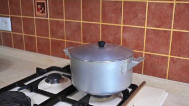 The cover moves away from the pressure of steam in the pan of boiling water on the stove in the home rustic wooden kitchen. Slow motion