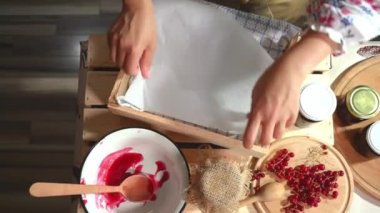 View from above of housewifes hands, putting inverted glass jars with freshly made berry jam in a wooden crate and covering them with waffle towel. Preparing homemade delicious red currant jelly