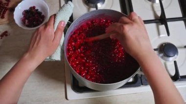 Sobanın başında dikilen bir şefin el kamerasının yakın plan videosu. Ev yapımı dut jölesi pişirirken ahşap kaşıkla kaynatılmış kırmızı üzümlü reçel karışımı. Yukarıdan görüntüle