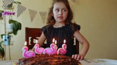 Sevimli bir çocuk, beyaz bir doğum günü kızı zarif bir donanma elbisesi giyiyor altın puantiyeli, dilek diliyor ve doğum günü pastasında mumlar üflüyor. Doğum günün kutlu olsun.