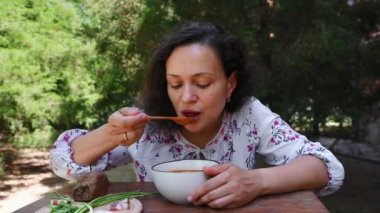 Ukrayna mutfağına aşina olan çok ırklı bir kadın, Ukrayna yemeği - borscht - yeşil soğanlı pancar çorbası, pastırma dilimleri ve Ukrayna kırsalında çavdar ekmeği yiyor.