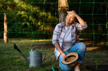 Enfes, genç, çoklu etnik kadın bahçıvan, çiftçi amatör, eko çiftliğindeki güzel günbatımına hayran. Yüzüne güneş ışınları düşüyor. Bahçecilik, tarım, organik tarım, bahçe işleri.