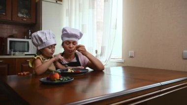 Steadicam shot. Multiethnic pretty woman housewife, loving mother sitting at wooden kitchen table with her adorable daughter- charming baby girl and tasting delicious balls of mango ice cream sorbet