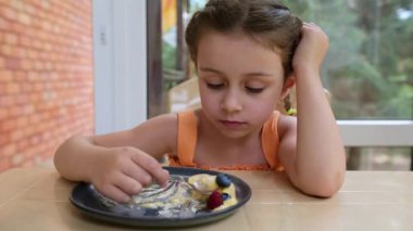 Close-up. Headshot of a beautiful Caucasian little girl finishing her delicious ice cream sorbet, melting on a ceramic plate, in the summer veranda. Child eating refreshing frozen dessert
