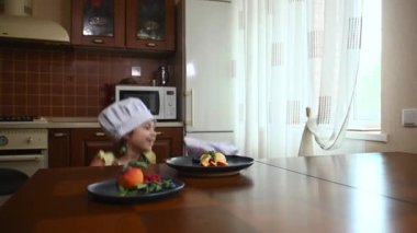 Cheerful mother and little daughter in confectioner uniform - chefs cap and aprons crawl out from under the table and are surprised to see a delicious dessert, ice cream balls on wooden kitchen table