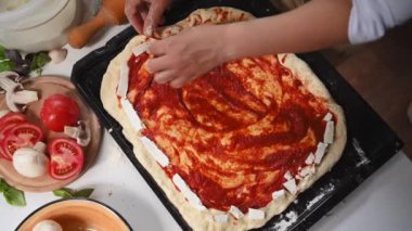 Top view: Hands of pizzaiolo chef putting feta cheese on the sides of the rolled out dough, preparing delicious Italian pizza with cheese sides in rustic kitchen. Traditional Italian cuisine. Close-up