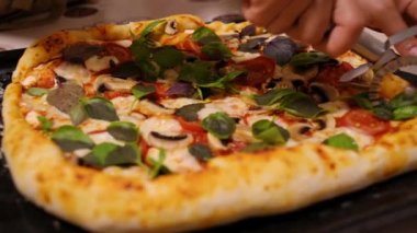 Close-up of the hands of a housewife using pizza wheels or cutter, cuts a homemade freshly baked pizza with organic vegetables and mozzarella cheese.