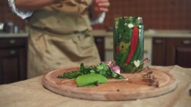 Close-up of a housewife in beige apron, putting a sterile lid on a glass jar of freshly pickled chili peppers. Homemade canned food. Preparing marinated delicacy for the winter season. Pickling.
