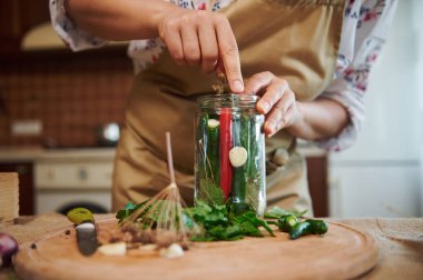 Close-up of a woman, putting peeled fresh garlic in the glass jar with fresh chili peppers, cooking marinated food, making preserved delicacies for the winter season at home kitchen. Pickling. Canning