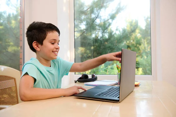 Handsome judicious smart schoolboy sits at the laptop, preparing for an online lesson during distance learning at home. Back to school. Online education. Homeschooling. Always open to new knowledge