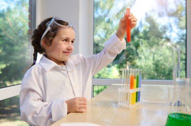 Caucasian preschooler girl testing chemical lab experiment and holding flask with orange liquid during chemistry lesson. Experiment science. New knowledge.