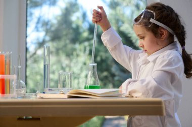Side view of a Caucasian little girl chemist using pipette, dripping reagents into a flask with chemical liquid in the school laboratory. Learning Science and chemistry in new academic year semester
