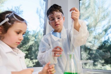Schoolboy using pipette, dripping few reagents in the flask with solution, making chemical experiments at chemistry class. Fascinating miraculous experiments for kids entertainment. Learning science
