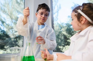European cute kids, boy and girl student child learn science, research and doing a chemical scientific experiment, analyzing and mixing liquid in flasks and test tubes on class at school laboratory
