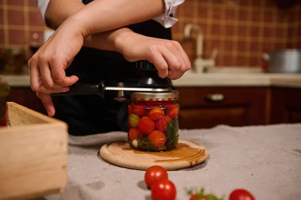 Process of preserving cherry tomatoes for the winter. Womens hands close the lids of jars with ripe red juicy organic tomatoes with a special key. Canning food according traditional family recipe