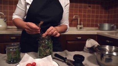 Steadicam shot of a housewife putting umbrella dill in canning jars, standing at the kitchen island and preserving seasonal vegetables for the winter. Salting, Canned food, pickling, marinating