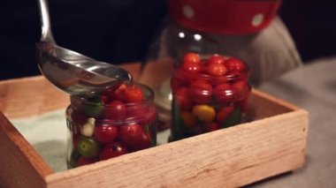 Close-up of pouring boiling marinade into jars with cherry tomatoes, marinated with pepper and fragrant culinary herbs, according traditional recipe. Canning. Preparing homemade fermented vegetable