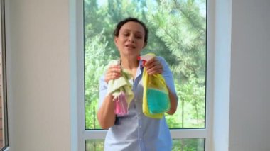 Multi-ethnic woman, pleasant positive housewife, maid singing songs and dancing with detergents sprays and rags in her hands, having fun while happily doing housework. Housekeeping. Household chores