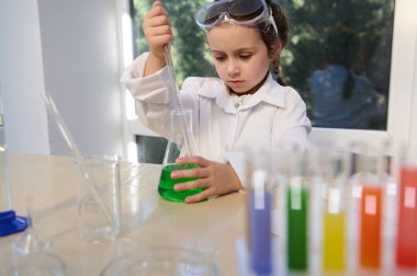 Little European preschooler girl making scientific experiments, fascinated and inspired by learning Chemistry. Science, chemical education concept. Back to school in the new academic year semester