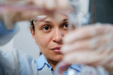 Focus on a female laboratory personnel, pouring pink liquid chemical substance from a glass flask through a funnel into a test tube, while conducting analyzes in a medical laboratory