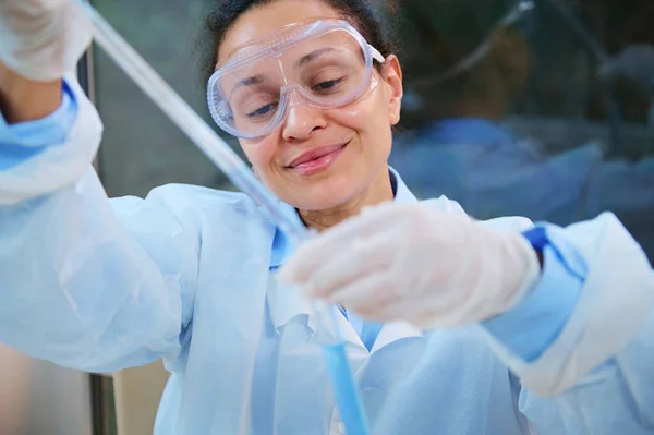 Pleasant experienced female scientist using a laboratory pipette, drips reagent into a test tube while conducting a clinical research and working on new vaccine in scientific biological laboratory