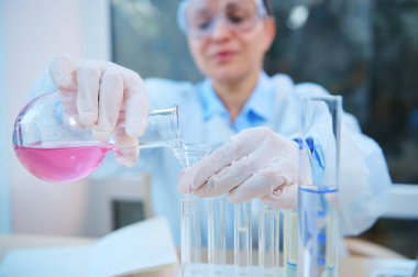 Close-up. Hands of a scientific researcher pouring liquid through a funnel from a glass laboratory flask into test tubes while making investigations and clinical researche in medicine and pharmacology