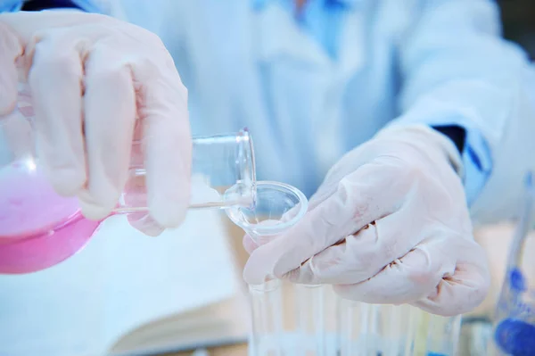 Close-up. Pouring pink liquid substance from a round bottom flask into a test tube using a glass laboratory funnel. Pharmacy and medicine. Clinical Study. Selective focus