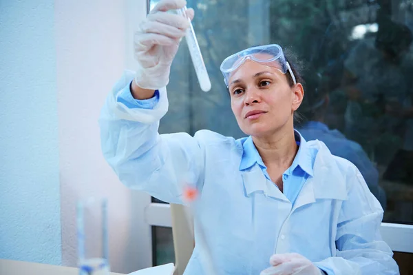 Caucasian woman scientist chemist, employee of a clinical research laboratory, experienced pharmacologist studies the properties of the drug in the test tube. Pharmacologist synthesizes a vaccine