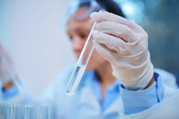 Selective focus on a test tube with a chemical in the hand of a blurred scientist, pharmacologist working on a new drug in a research laboratory. Pharmacy and medicine. Clinical Study