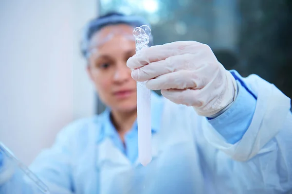 Details: A test tube in the hands in protective gloves of a blurred background of a scientist pharmacologist examining the taking place chemical reaction in a science clinical research laboratory