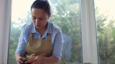Close-up of a multi-ethnic woman, florist gardener working with fertilized soil, planting and cultivating plants. Floriculture. Gardening. Household chores