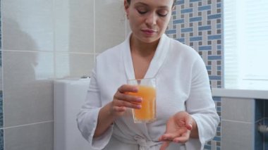 Close-up portrait of a multi-ethnic pretty woman in white bathrobe, drinking water with effervescent antioxidants, minerals, vitamins and nutritional supplements, according to physicians prescription