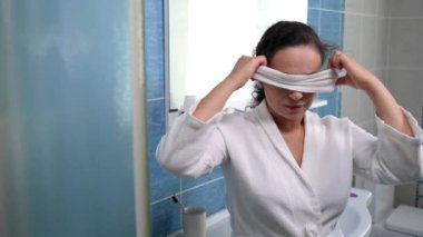 Attractive middle-aged pretty woman in white waffle bathrobe, putting on a terry headband during daily morning beauty skin and body care procedures in the bathroom. Hygiene. Purity. Healthy lifestyle