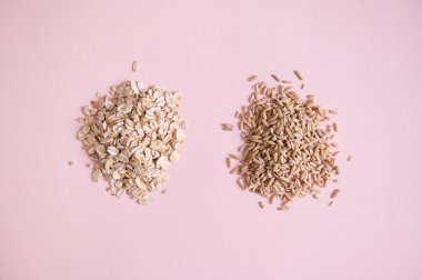 Flat lay. Heap of oatmeal groats and oat-flakes scattered on pink background with copy space. Vegan wholesome ingredients for making plant based milk, alternative dairy free vegan drink. Veganism.