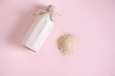 Flat lat. Still life with a heap of white rice and glass bottle of plant based, organic, healthy rice milk, on pink surface with copy advertising text. Vegan wholesome dairy free drink. Healthy eating