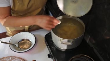Top view of a housewife throwing dumplings with potatoes into boiling water and stirring them with a kitchen spoon during cooking. Preparing traditional Ukrainian dish- Vareniki in the country kitchen