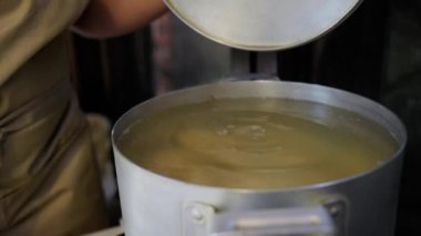 Selective focus on metal saucepan on electric stove, and housewife's hand throwing homemade dumplings, ravioli, pelmeni, vareniki into a boiling water. Traditional cuisine. Culinary and baking concept