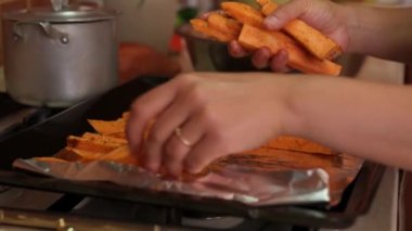 Yakın plan kadın şeflerin elleri, fırında pişirmeden önce üzerine biberiye yaprakları süsleyerek, bir folyoya tatlı patates takozu koyuyor. Yemek pişirme süreci konsepti. Sağlıklı vejetaryen yemeği