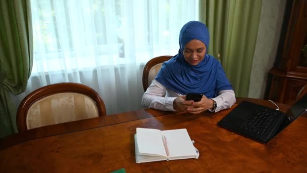 用手机 滚动新闻资料 浏览网站 查看社交媒体上的内容 撰写讯息 俯瞰一位头戴头巾 头戴正式服装 自信的年轻阿拉伯穆斯林女性 — 图库视频影像