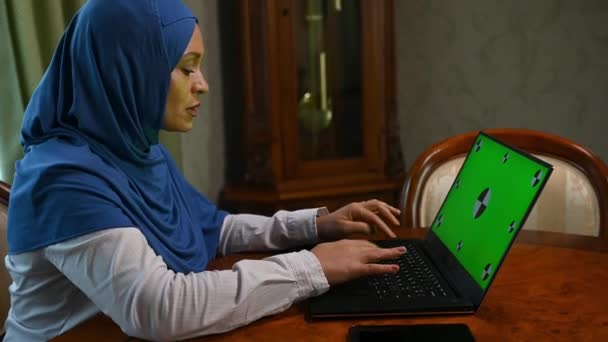 勤勉なイスラム教徒中東のビジネス女性ヒジャーブでは キーボードにテキストを入力し 緑のクロマキーでノートパソコン上でリモートで作業しながら コンピュータプログラムを書き込みます 広告クリップのためのモックアップ画面 — ストック動画